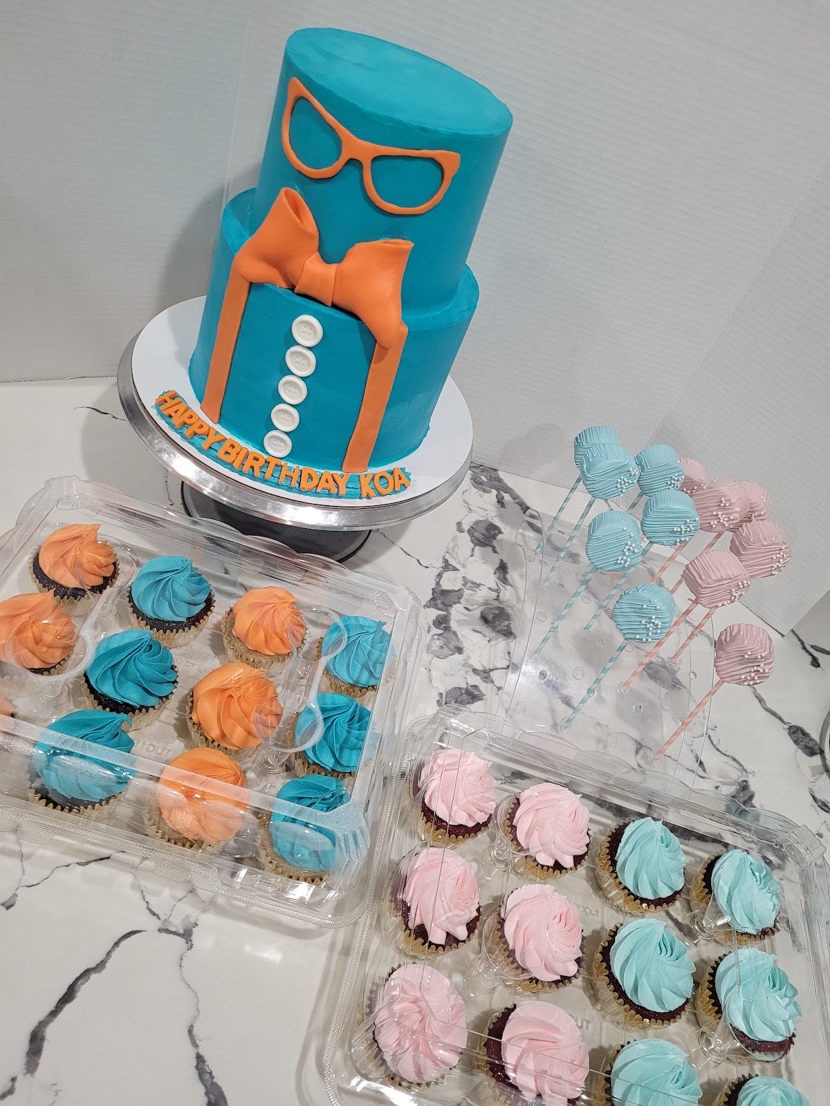 Two tier teal and orange bow tie cake with matching cupcakes and cake pops