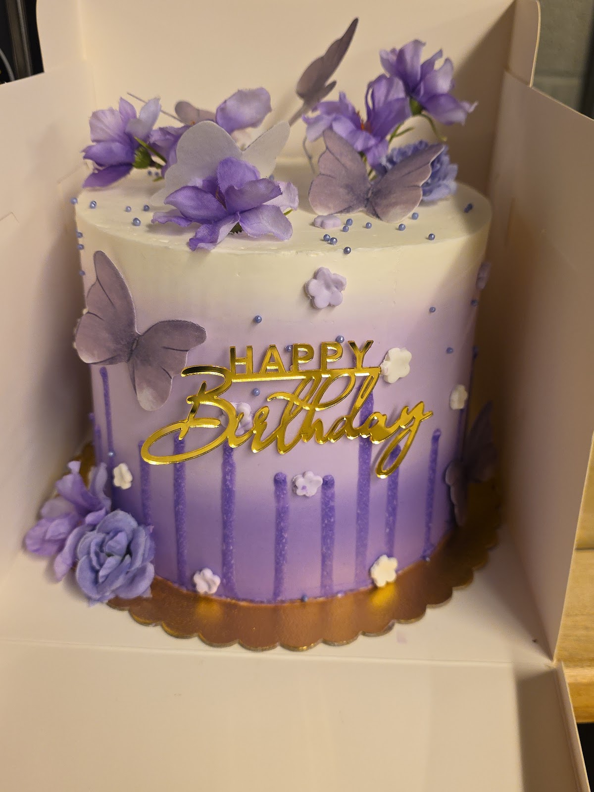 Purple ombre drip cake with butterflies, florals and a gold Happy Birthday topper